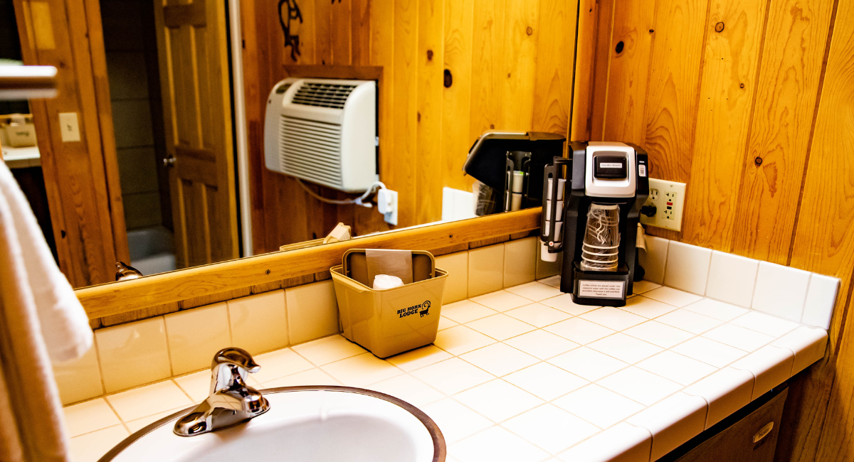 A bathroom sink with a mirror, coffee maker, and wood paneling
