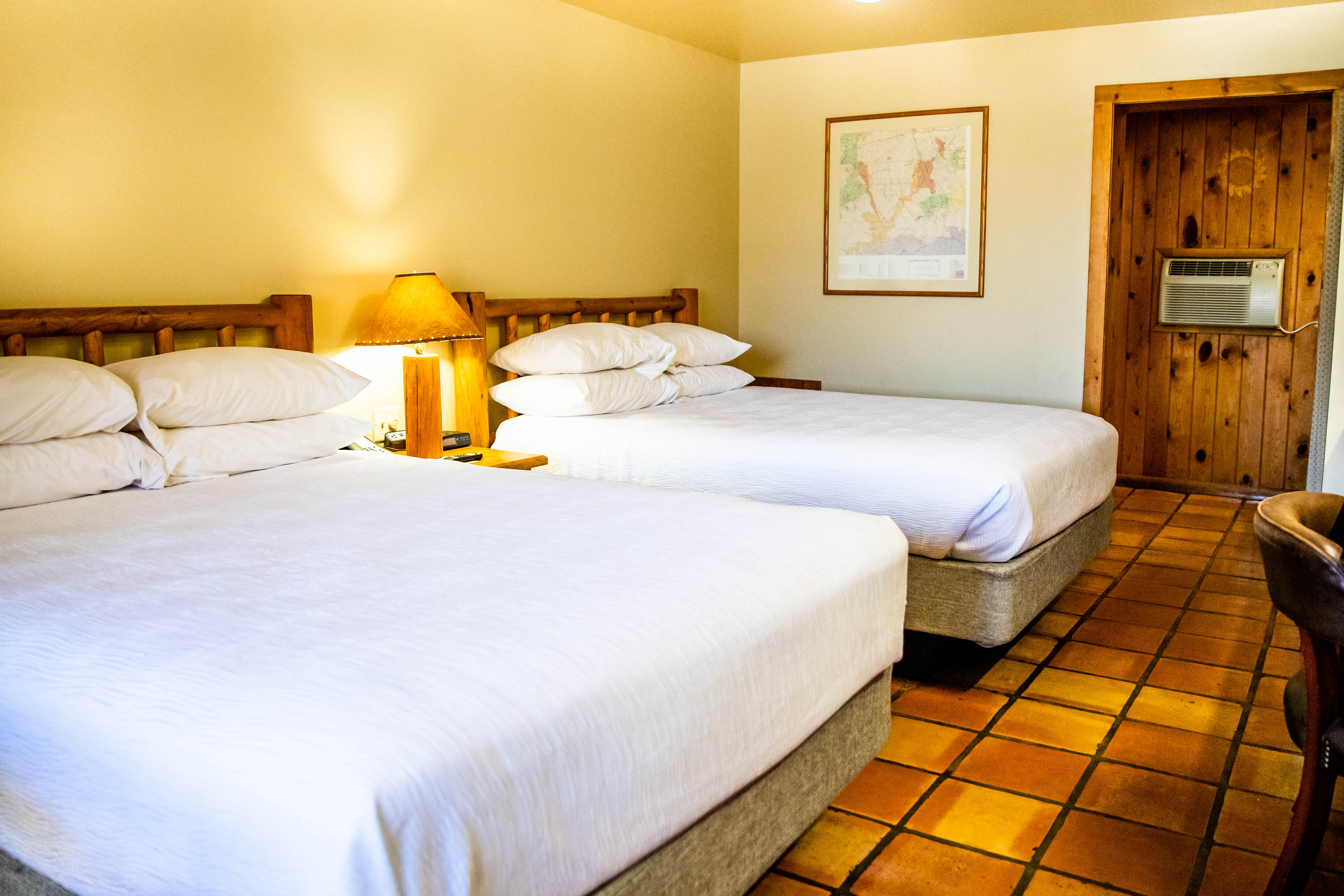 A hotel room with two queen beds, wooden headboards, and a tiled floor.