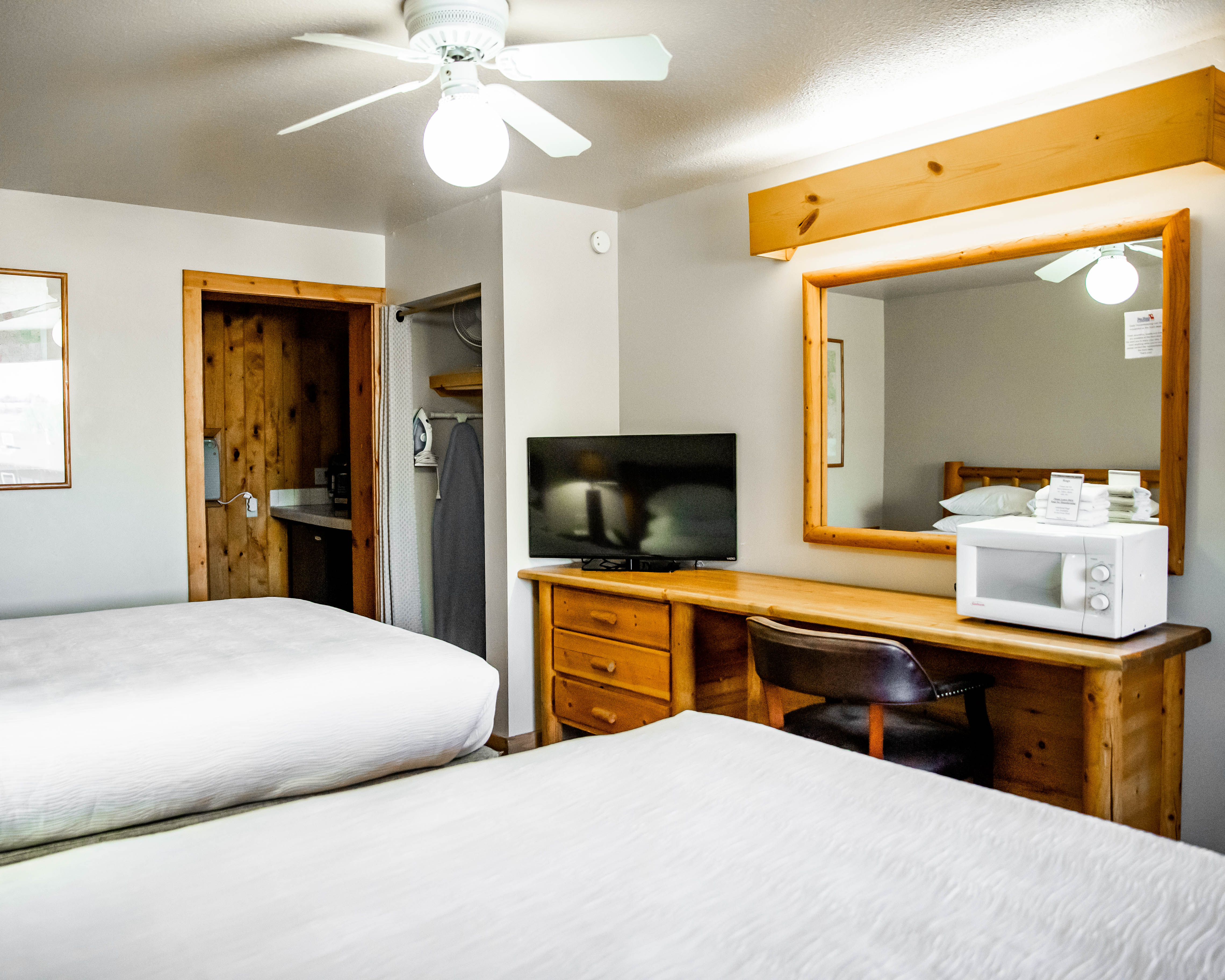 A hotel room with two queen beds, a wooden desk with a microwave and TV, and a large mirror.